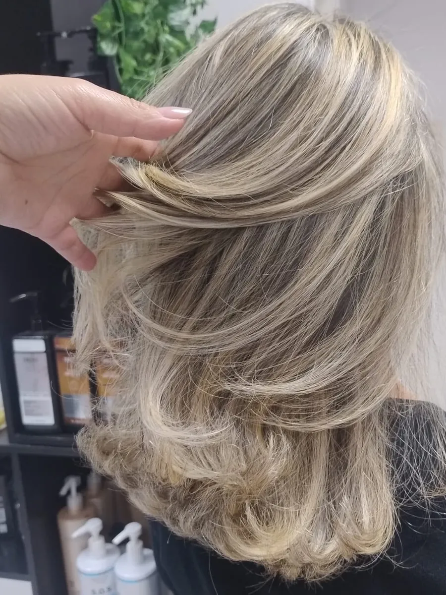 Mão da cabeleireira mostrando mechas loiras em camadas
